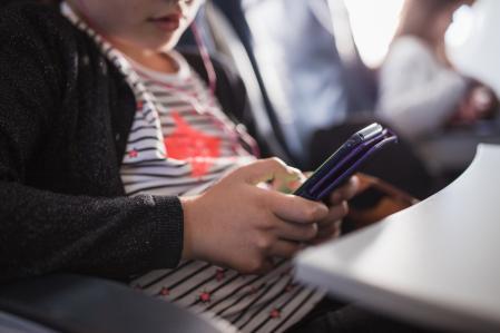Close-up of a young girl sitting in airplane and using smartphone with in-ear headphones