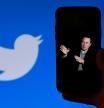 Elon Musk, whose photograph on a mobile seems to point to the Twitter logo in the background of the image