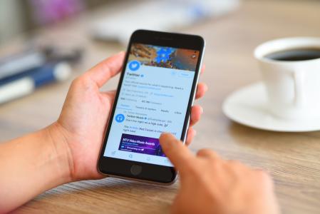 İstanbul, Turkey - August 28, 2017: Woman using smart phone on a wooden desk. The smart phone is an iPhone 6 plus displaying Twitter application.  iPhone is a touchscreen smartphone developed by Apple Inc.