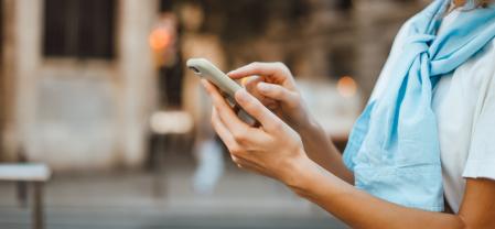 Close-up photo of female hands with smartphone. Young woman typing on a mobile phone on a sunny street