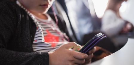 Close-up of a young girl sitting in airplane and using smartphone with in-ear headphones